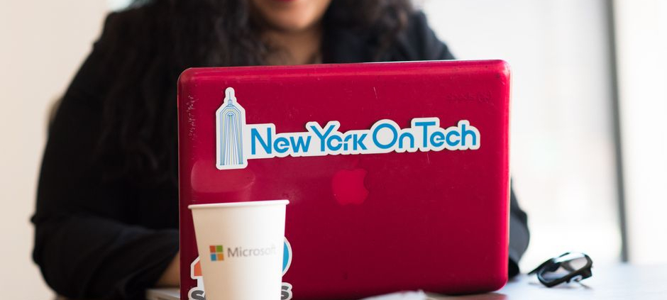 Young woman working remotely with a laptop in a modern indoor office setting, showcasing tech culture.