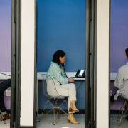 Business professionals using phone booths for communication in a modern office space.
