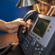 A close-up image of a hand picking up a handset from an office telephone, emphasizing communication device usage.