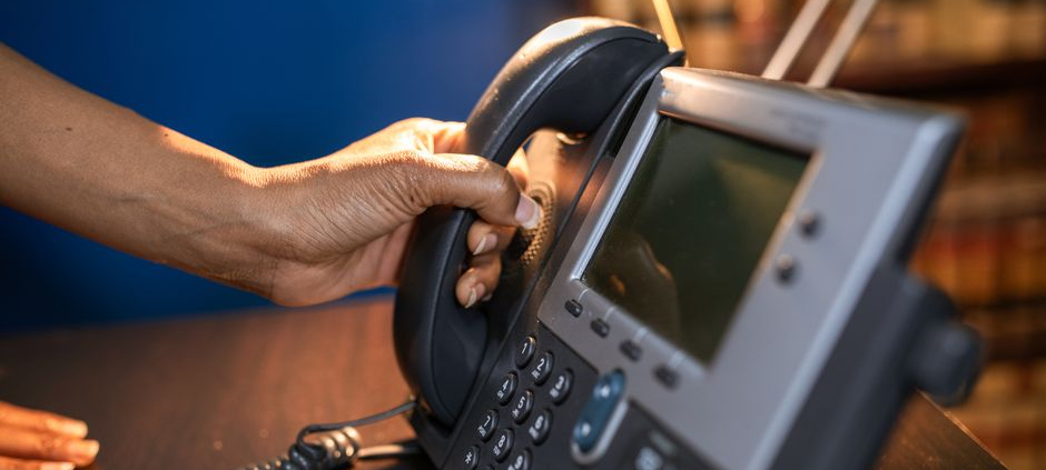 A close-up image of a hand picking up a handset from an office telephone, emphasizing communication device usage.