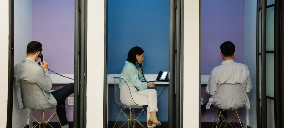 Business professionals using phone booths for communication in a modern office space.
