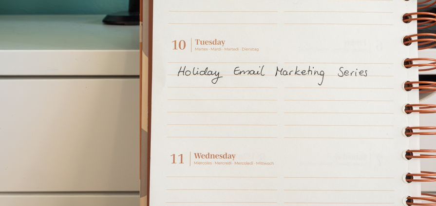 Planner open on a desk with handwritten 'Holiday Email Marketing Series' note.
